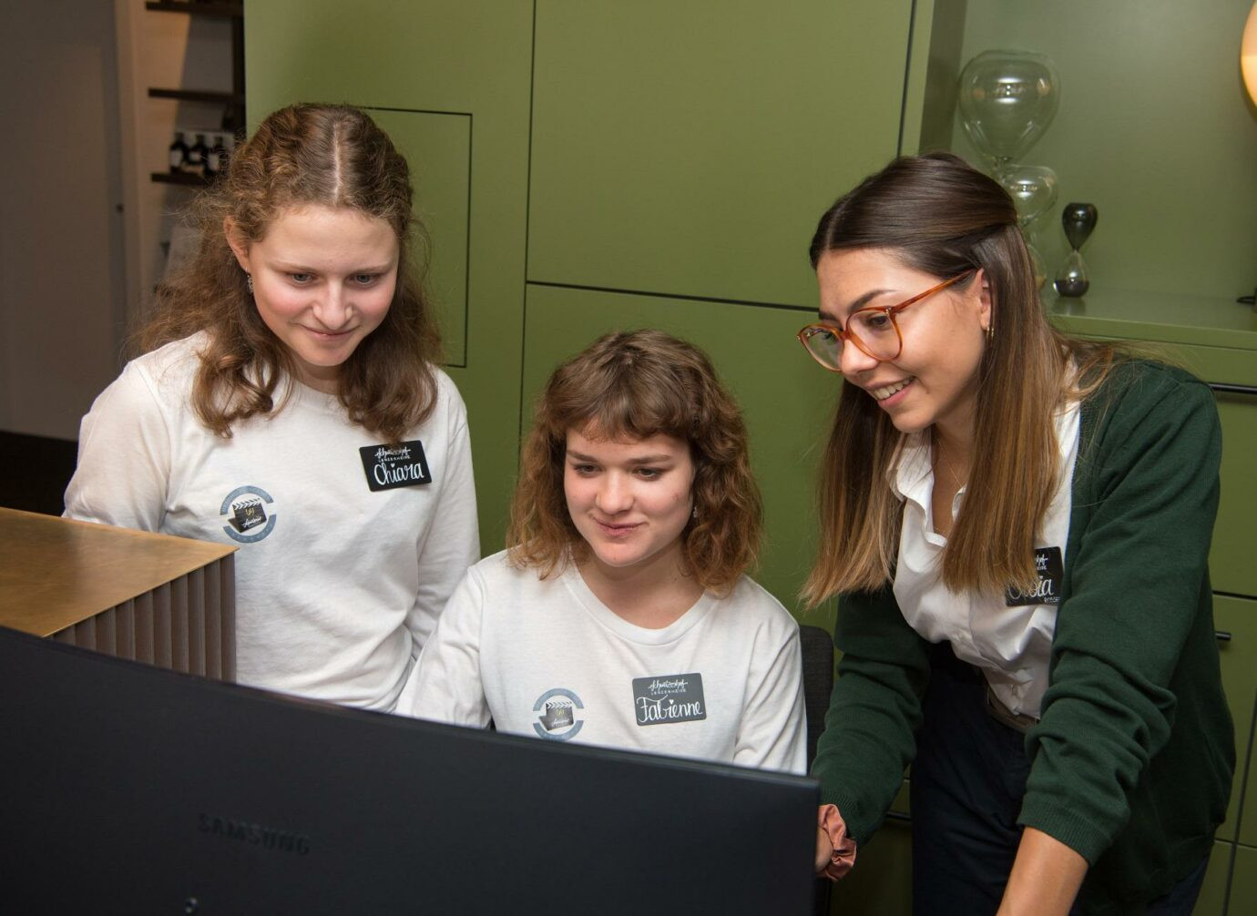 Eine Mitarbeiterin erklärt zwei Kindern etwas am Computer.