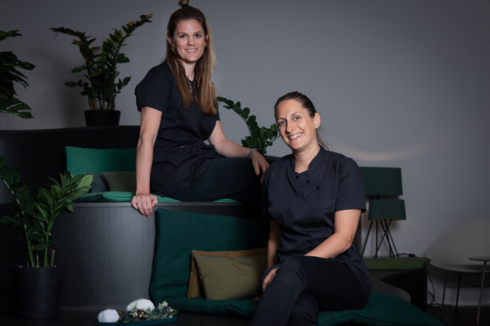 Zwei Spa-Mitarbeiterinnen im Hotel Schweizerhof Lenzerheide posieren lächelnd im Wellnessbereich.