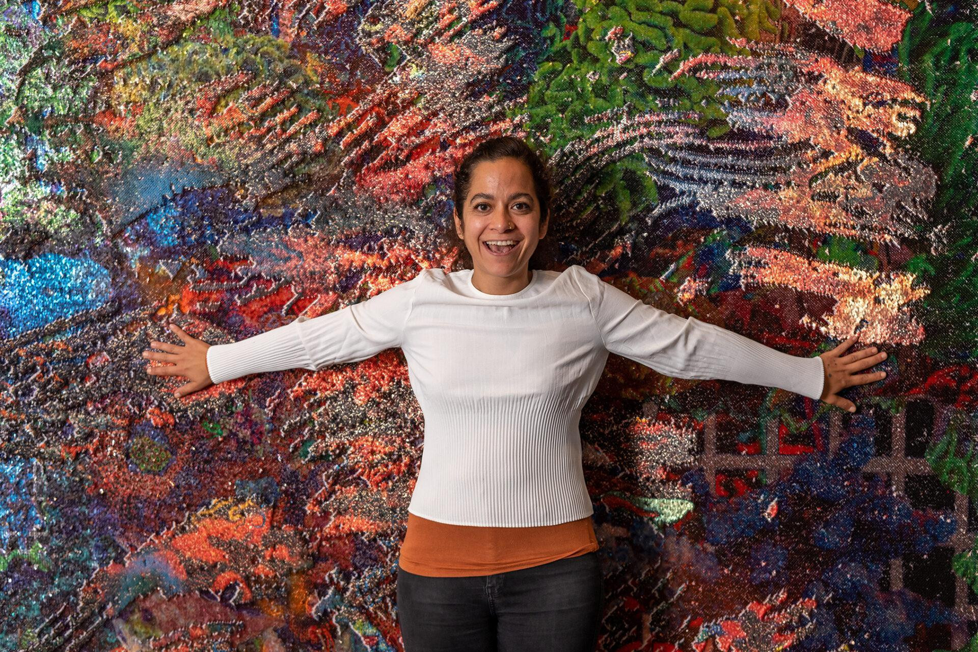 Frau die vor einem Kunstwerk steht und beide arme ausgestreckt hat.