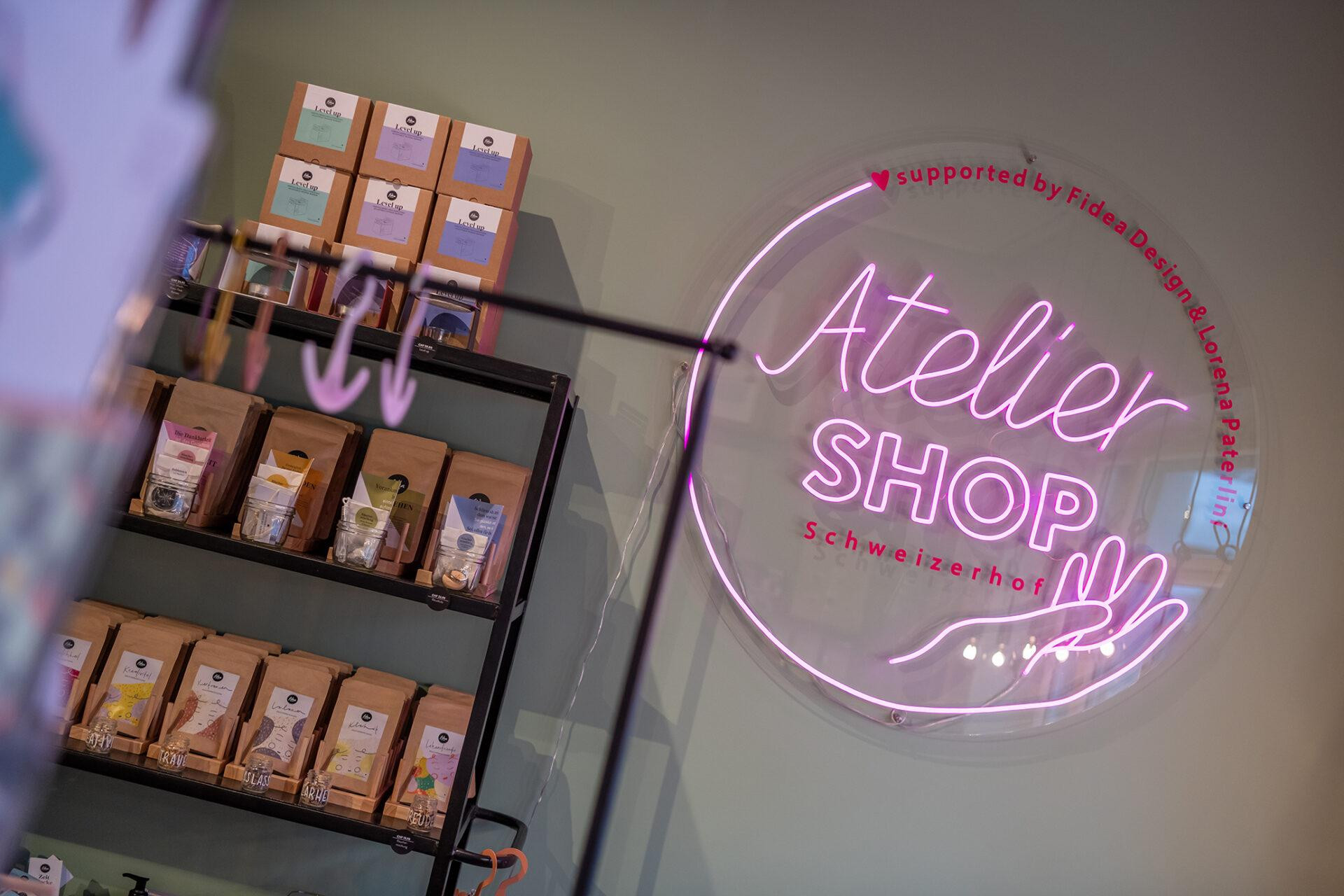 Einblick in den Atelier Shop von Lorena Paterlini. Links ein Regal mit Produkten und Rechts ein Neonlichter Schild.