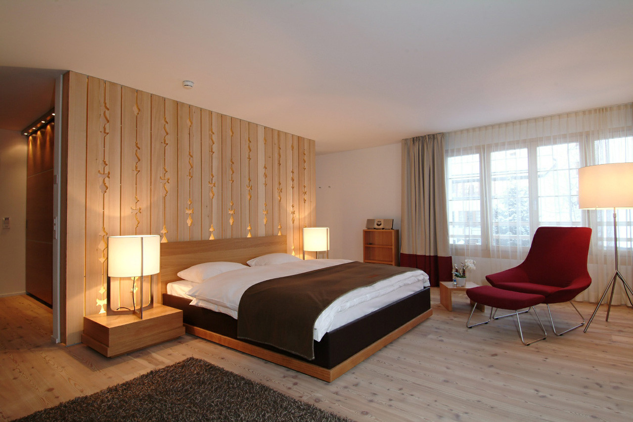 Alpenchic Suite mit gemütlichem Doppelbett, warmen Holzelementen und rotem Lounge-Sessel.