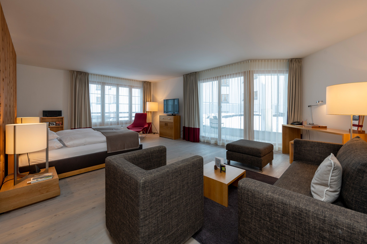 Grosszügige Alpenchic Suite mit Doppelbett, gemütlicher Sitzecke und grossen Fensterfronten.