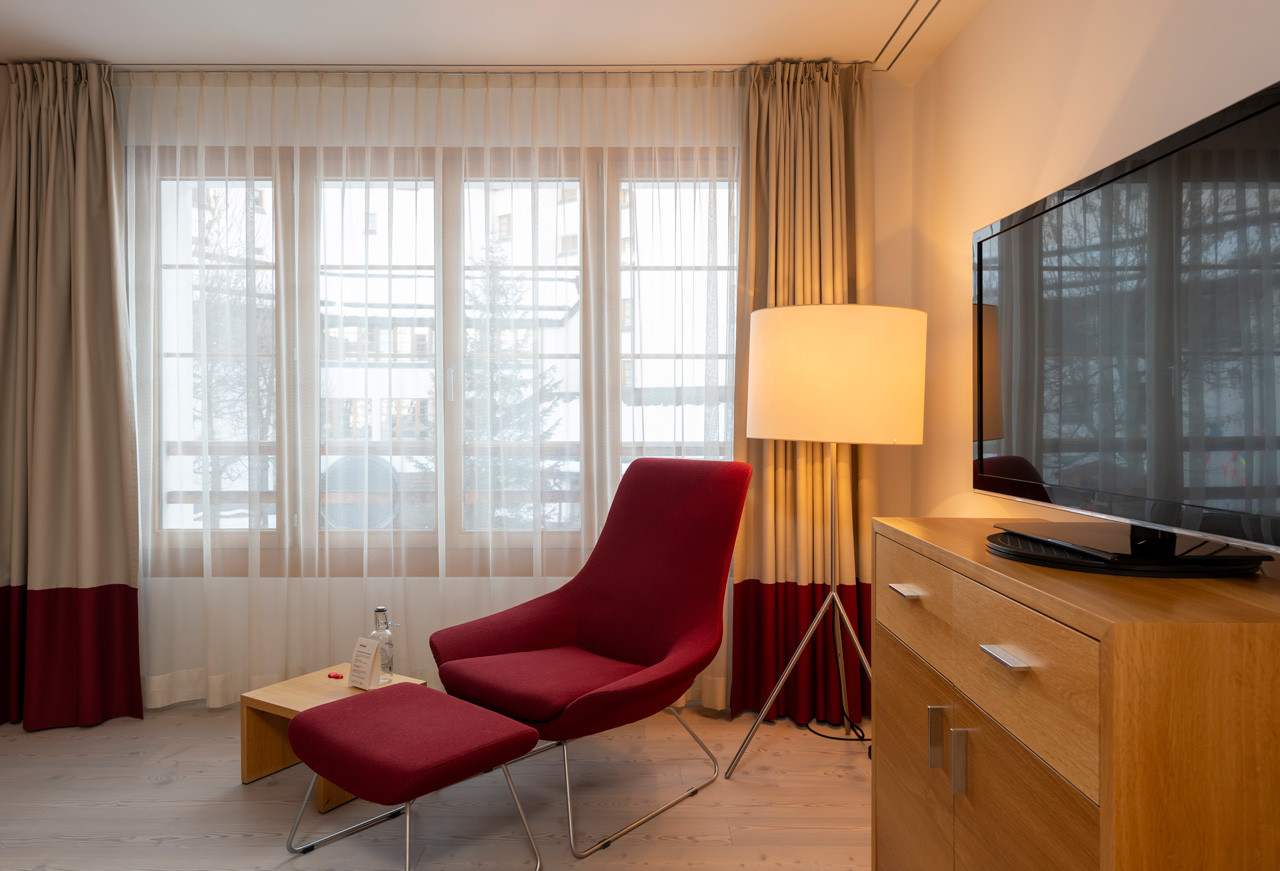 Sitzecke mit Rotem Sessel mit einer Kommode mit einem Fernseher mit grosser Fensterfront.