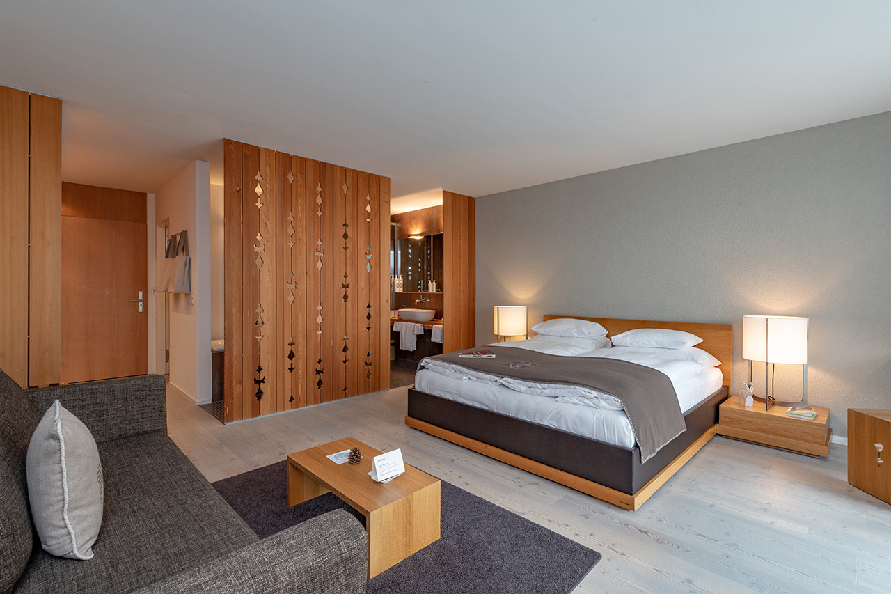 Modernes, helles Hotelzimmer mit grossem Doppelbett, Sitzbereich und Holzakzenten.