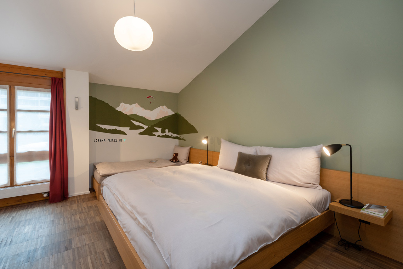 Budget Zimmer mit gemütlichem Doppelbett, Wandillustration im Alpenstil und hellem Tageslicht und mit einer Wandzeichnung von Bergen von Lorena Paterlini.
