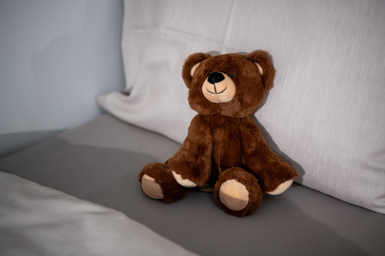Ein Teddybär der auf dem Bett sitzt.