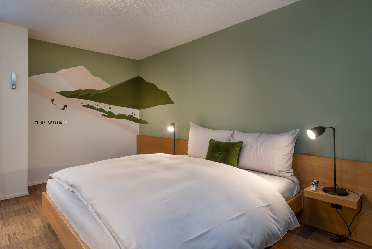 Budget Zimmer mit gemütlichem Doppelbett und Wandillustration mit alpinen Skimotiven.