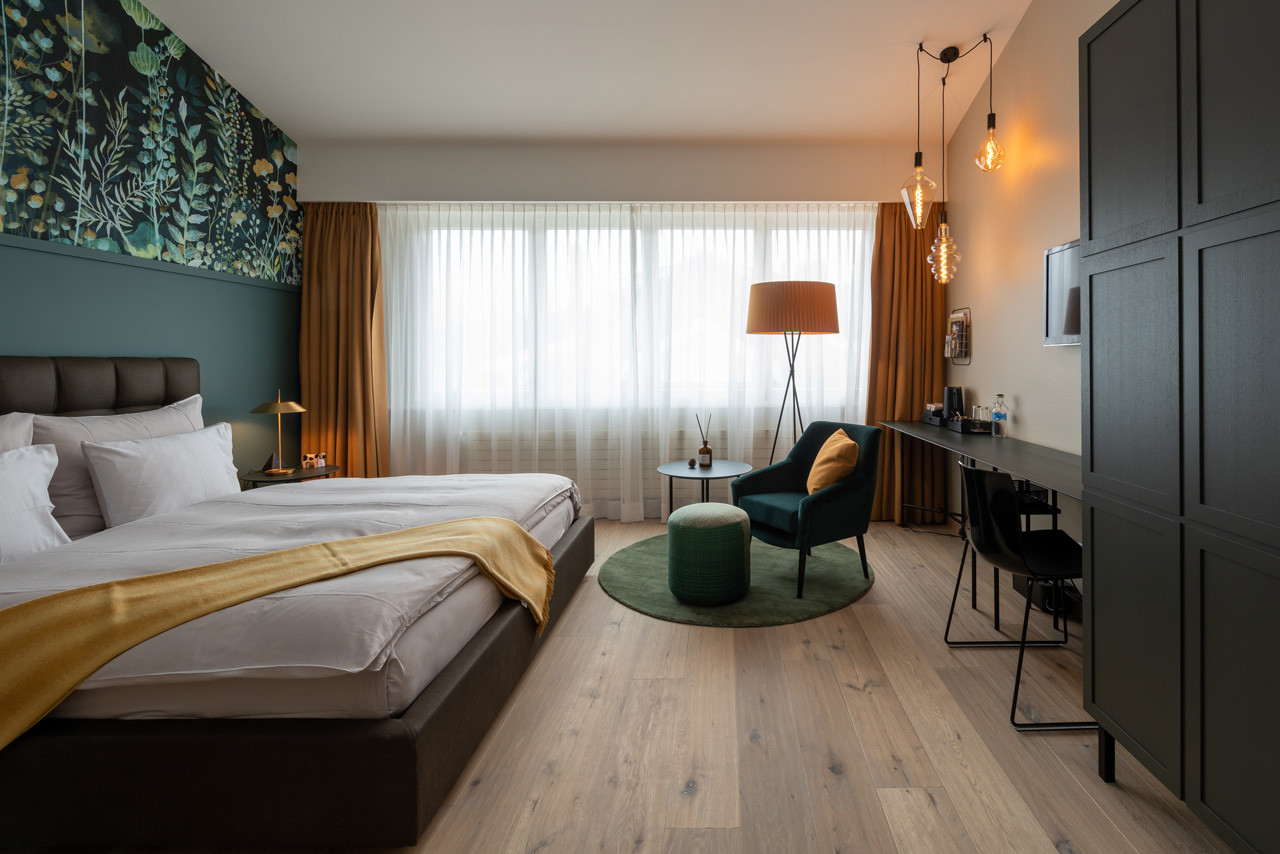 Nostalchic Belle Étage Zimmer mit elegantem Doppelbett, stilvoller Sitzgruppe und warmem Tageslicht sowie Kleiderschrank und Schreibtisch.