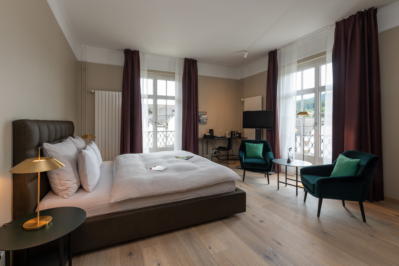 Nostalchic Zimmer mit elegantem Doppelbett, gemütlicher Sitzgruppe und grossen Fenstern mit viel Tageslicht.