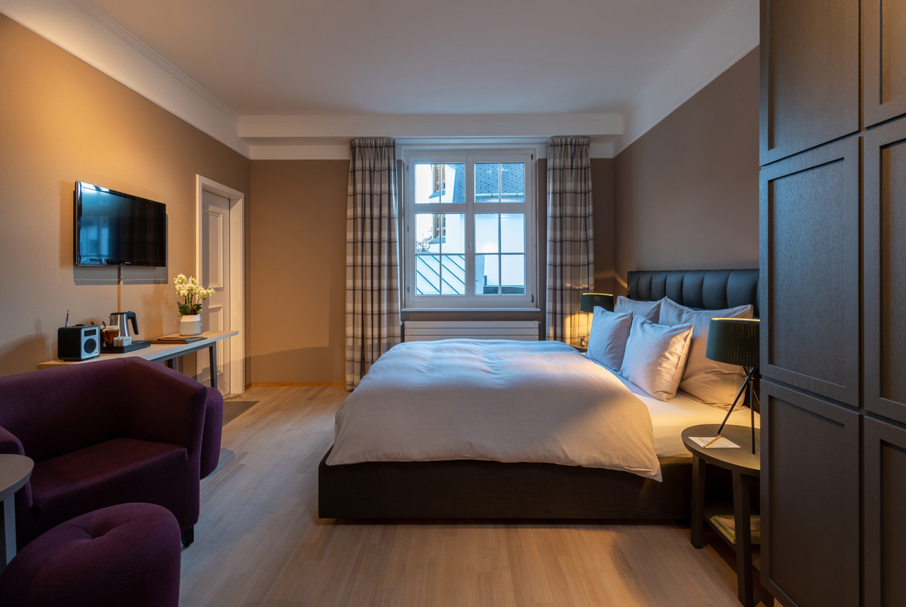 Nostalchic Zimmer mit elegantem Doppelbett, gemütlicher Sitzgruppe und grossen Fenstern mit viel Tageslicht.