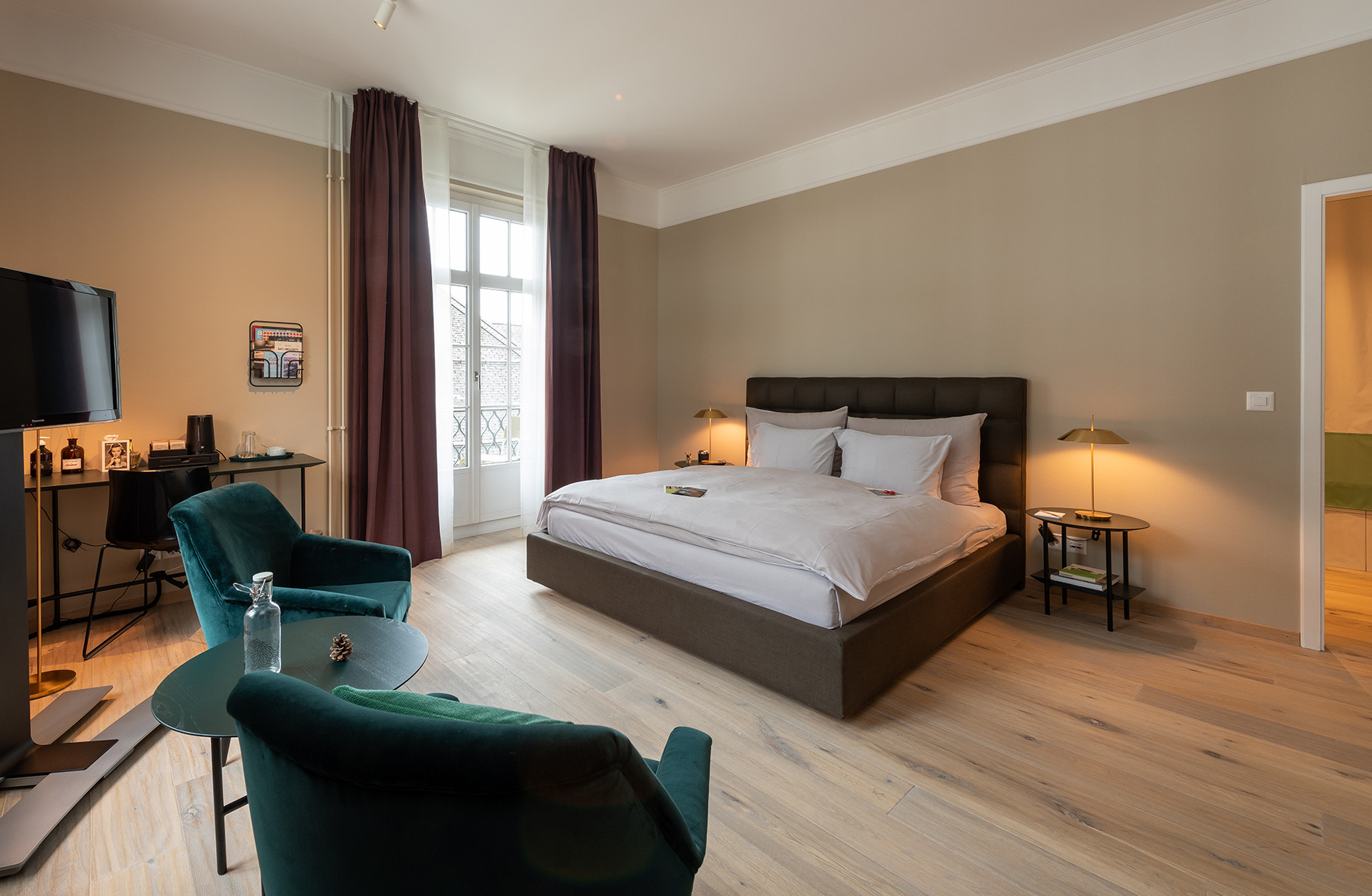 Nostalchic Zimmer mit elegantem Doppelbett, warmen Naturtönen und gemütlicher Sitzgruppe am Fenster.